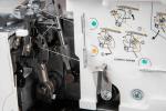 Nahaufnahme des Einfädelmechanismus der Gritzner 788 Overlock – 2/3/4-Faden mit Freiarm und LED, mit Anleitungsdiagrammen, farbigen Führungen, teilweise eingefädeltem weißem Faden und sichtbarem